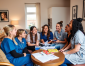 A group of nurses in scrubs engaged in discussion around a table filled with books and materials in a cozy room.